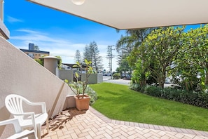 Eine Terrasse mit einem weißen Stuhl, einem Blumentopf und Blick auf eine Straße mit Gebäuden und Bäumen.