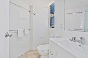 A modern bathroom with a walk-in shower, a toilet, and a sink with a mirror. - Sandown Right on Mermaid Beach (Gold Coast)