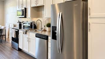 Une cuisine moderne dotée d’appareils électroménagers en acier inoxydable, de meubles blancs et d’un plancher en bois.
