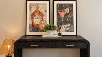 A black console table with two framed artworks, a small potted plant, and a book titled 'The Art of Home' on top.
