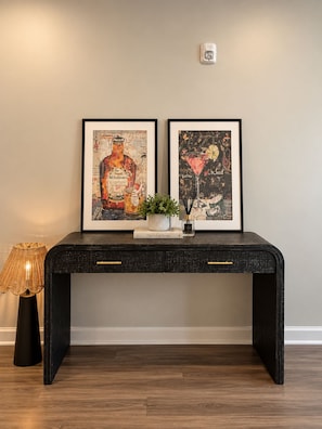 Eine schwarze Konsole mit zwei gerahmten Kunstwerken, einem kleinen Topfpflanzen und einem Buch mit dem Titel 'The Art of Home'.