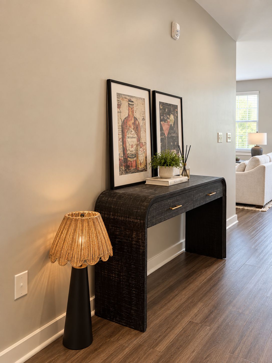 Una sala moderna con un mueble consola de madera oscura, una lámpara de mimbre y dos obras de arte enmarcadas en la pared.