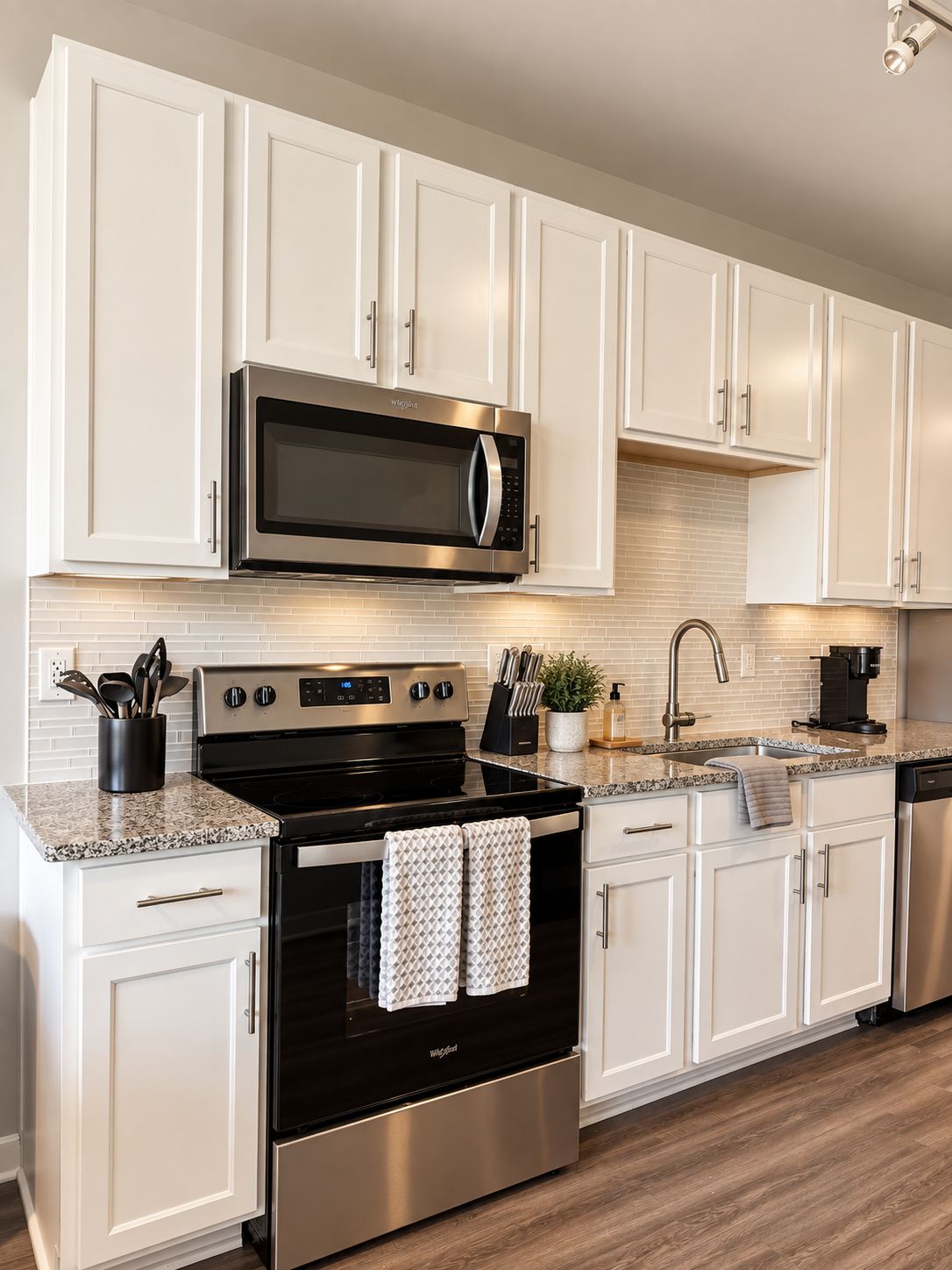 Una cocina moderna con muebles blancos, electrodomésticos de acero inoxidable, encimera de granito y salpicadero de azulejos.