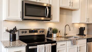 Una cocina moderna con muebles blancos, electrodomésticos de acero inoxidable, encimera de granito y salpicadero de azulejos.