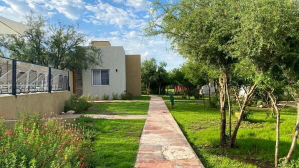 A pathway leading to a building with a window, surrounded by greenery and a fence. - Morada del Cóndor - Cabañas Serranas (Merlo)