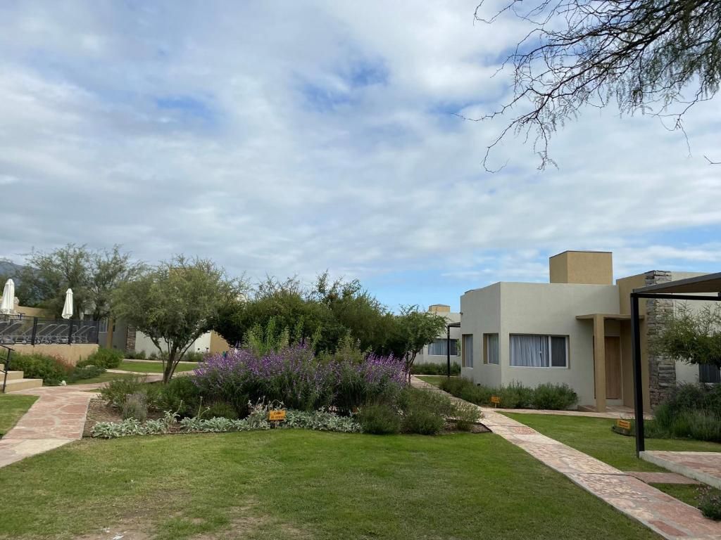 A modern building with a flat roof, surrounded by a well-maintained garden with various shrubs and a paved walkway.