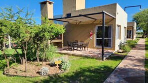 A modern building with a covered patio area, outdoor seating, and a garden. - Morada del Cóndor - Cabañas Serranas (Merlo)