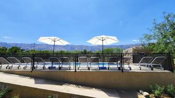 A poolside area with lounge chairs and umbrellas, a pool, and mountains in the background.