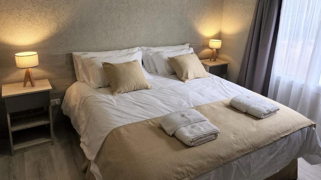 A hotel room with a bed, two bedside tables with lamps, and a window with curtains.