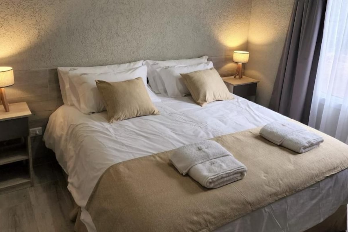 A hotel room with a bed, two bedside tables with lamps, and a window with curtains.