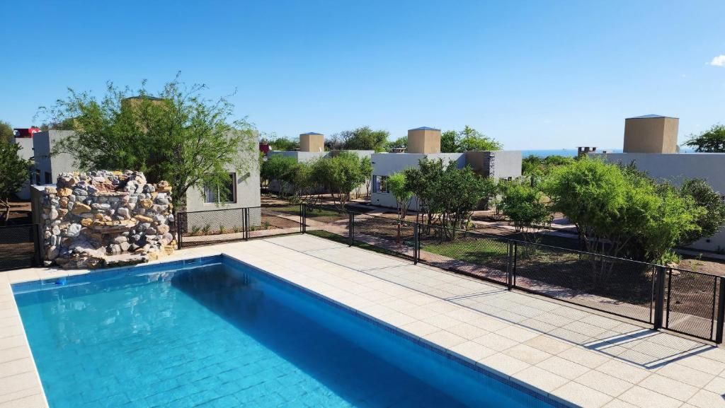 A swimming pool with a stone structure, surrounded by a fenced area with trees and buildings in the background.