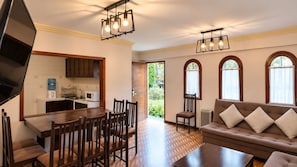 A living room with a brown sofa, wooden dining table, and chairs, a kitchen with white cabinets, and a large window with curtains. - Hotel Calacoto (La Paz)