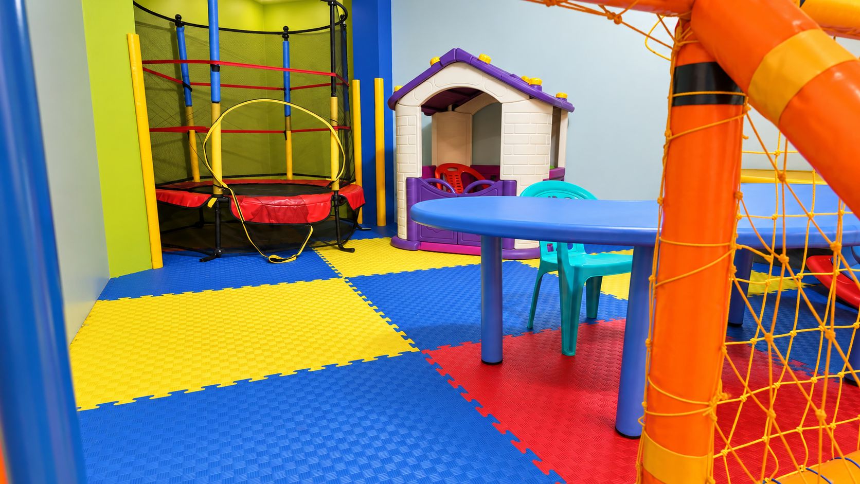 Zona de juegos con un trampolín, una casita y red de seguridad.