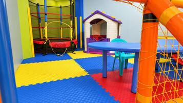 Zona de juegos con un trampolín, una casita y red de seguridad.