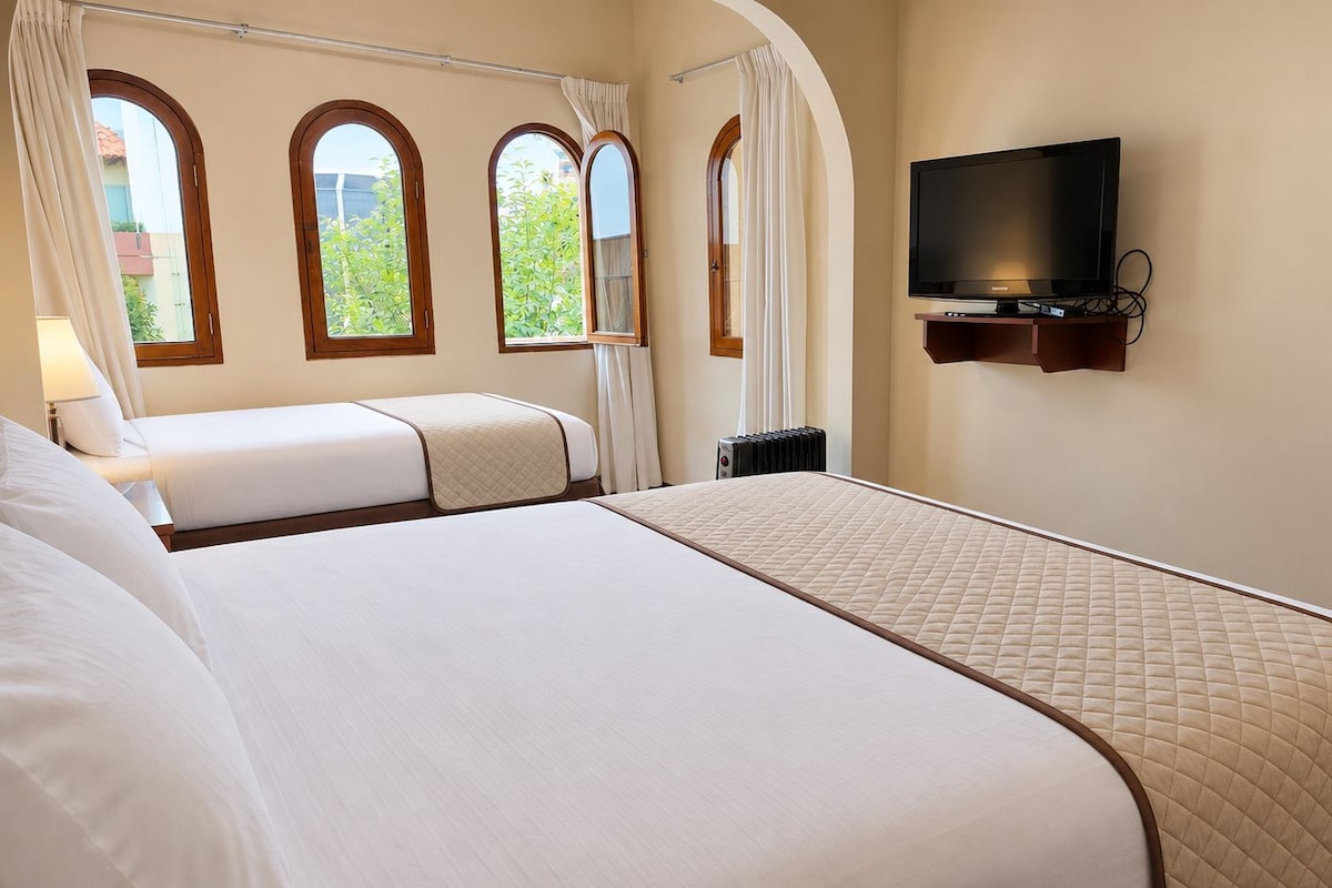 A hotel room with two beds, a television mounted on the wall, and a window with curtains.