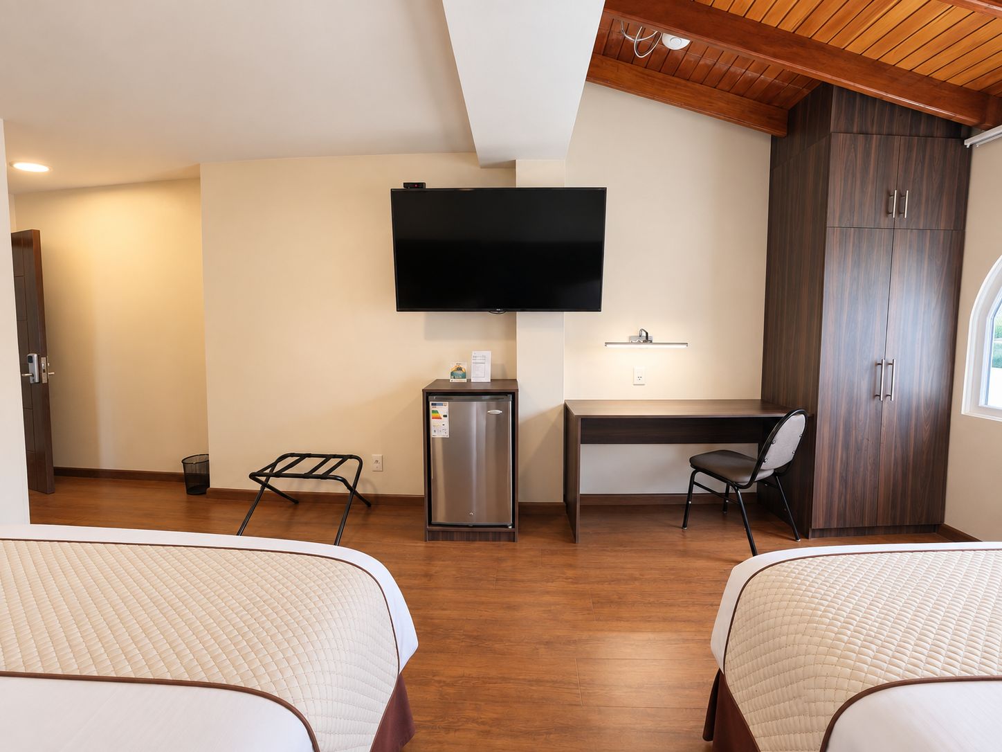Habitación de hotel con dos camas, un escritorio, televisión, minibar y armario.