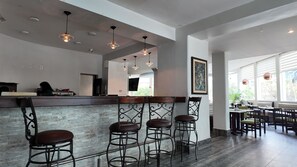 A bar area with a high counter, multiple stools, pendant lighting, and a view of the outdoor seating area. - Hotel Calacoto (La Paz)