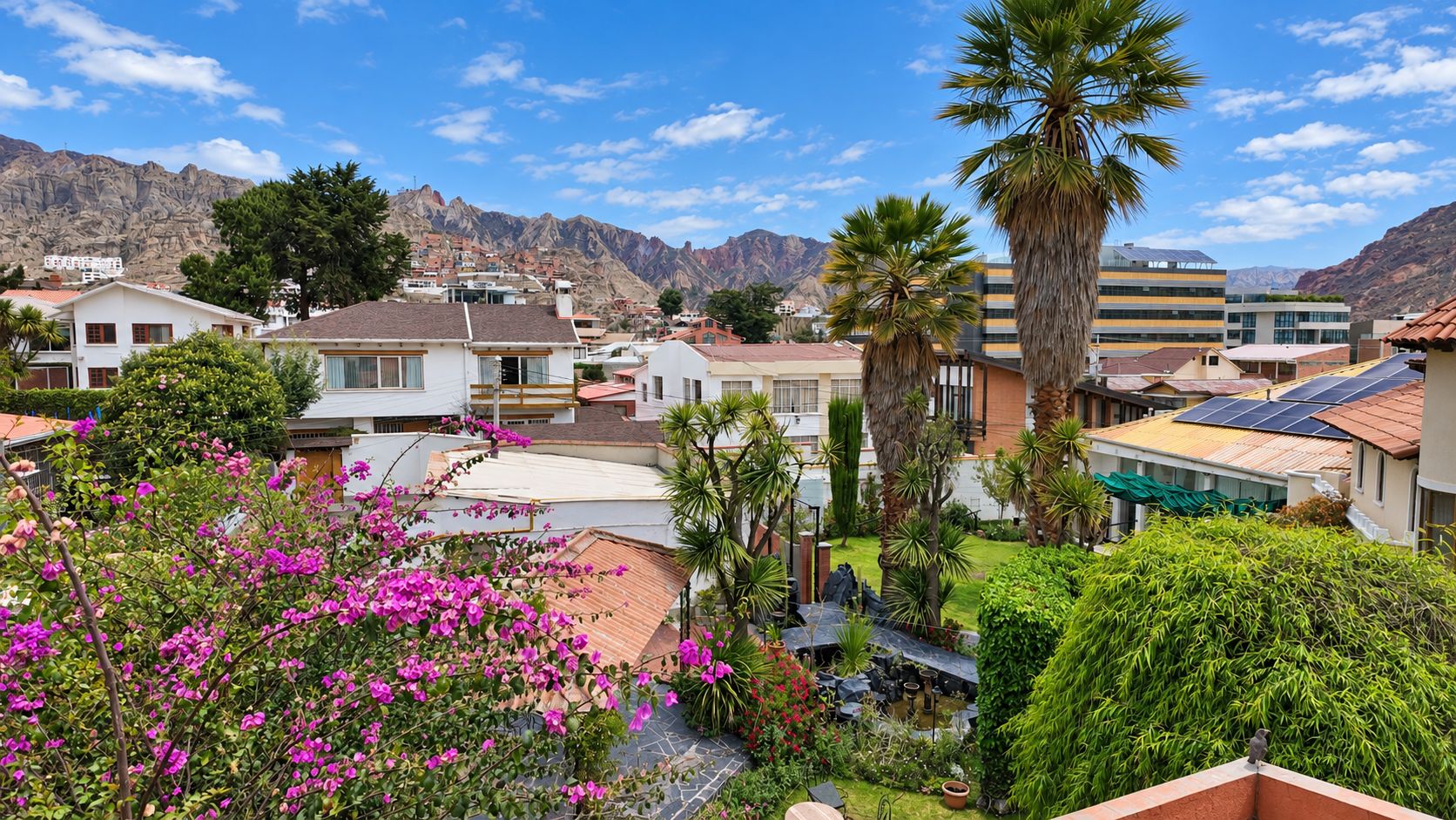 A residential area with houses, a large palm tree, and mountains in the background.