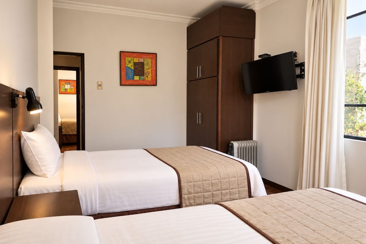 A hotel room with two beds, a wardrobe, a television, and a window with curtains.