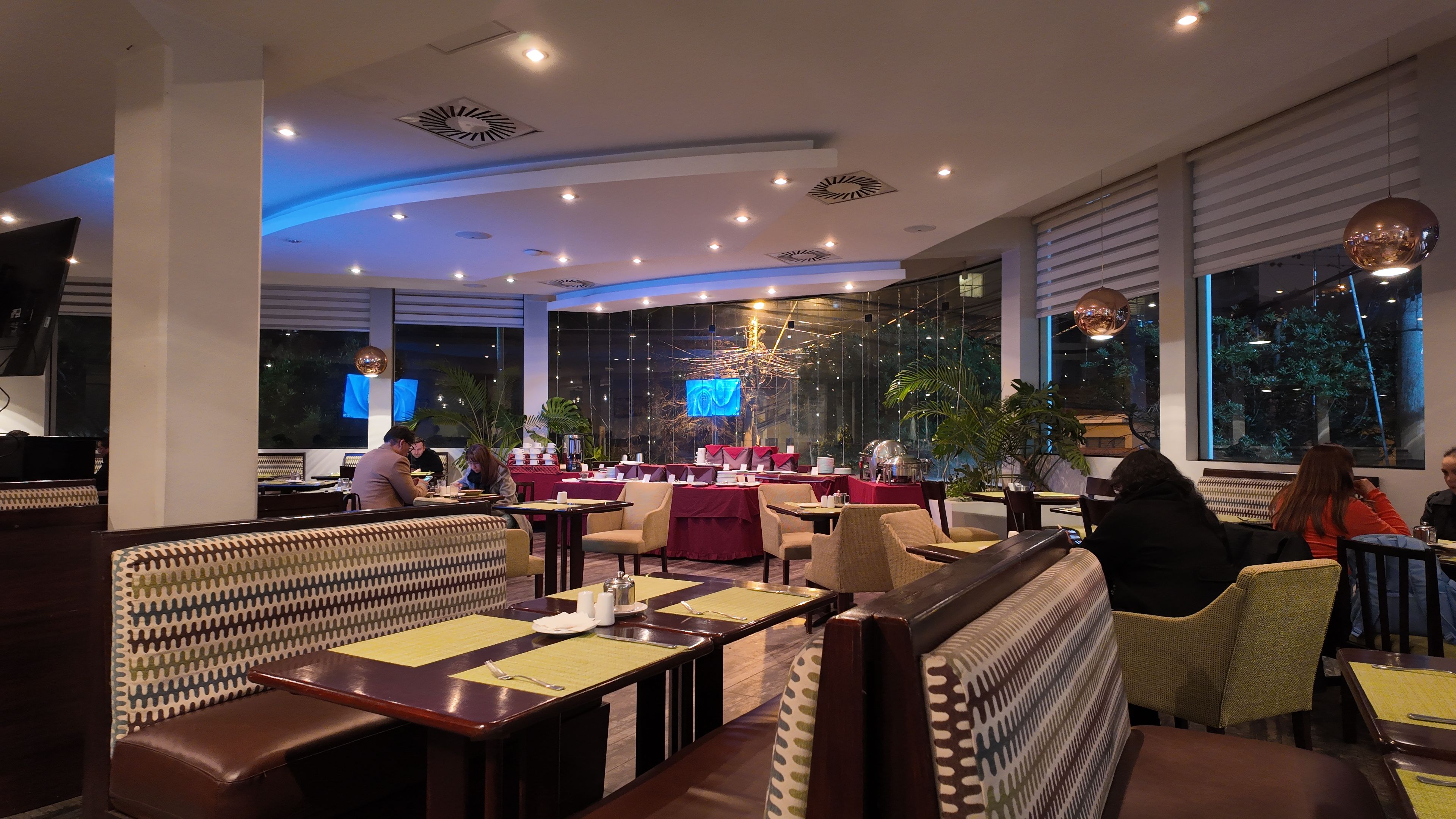 A restaurant with booths and tables, large windows, and indoor plants.