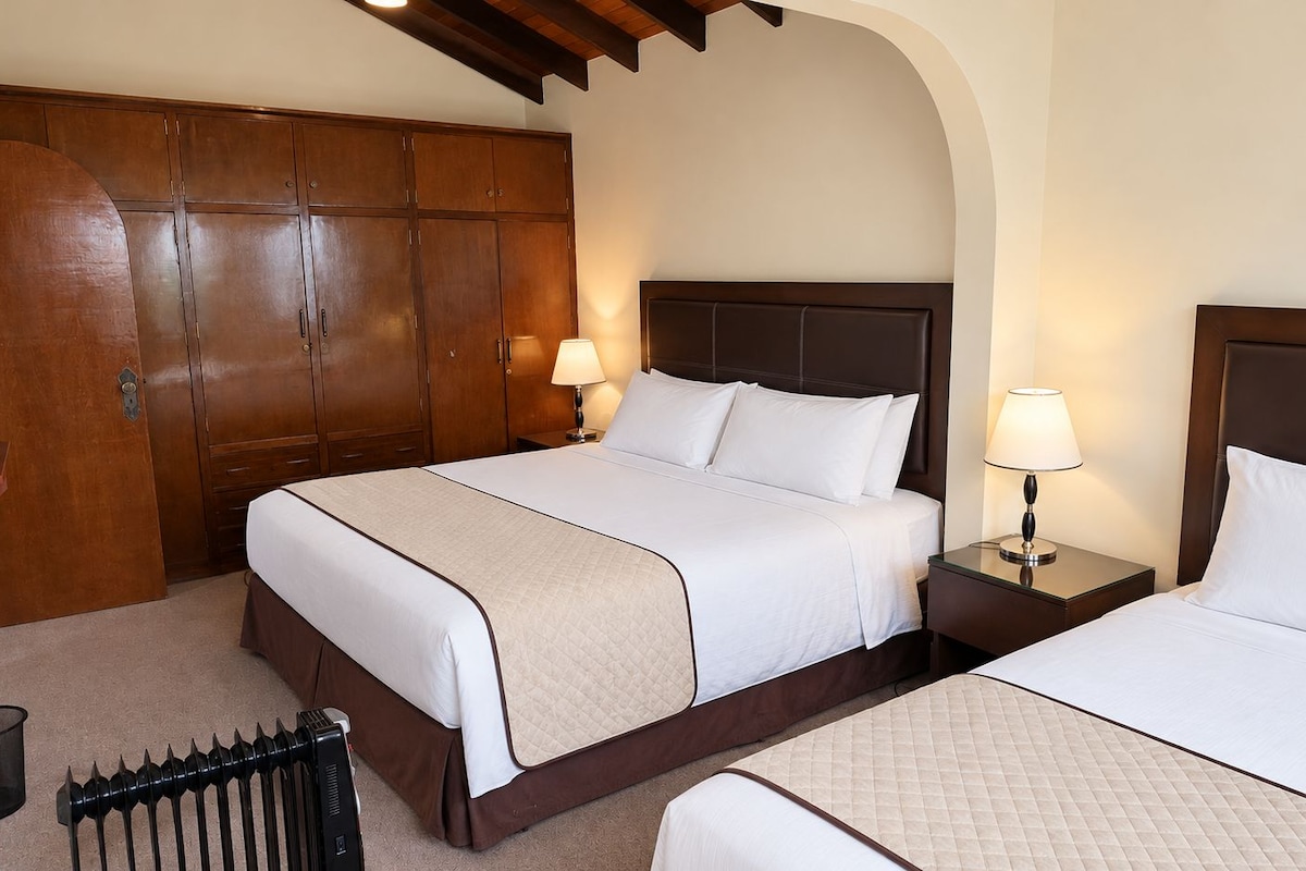 A hotel room with two beds, wooden wardrobe, and a radiator.