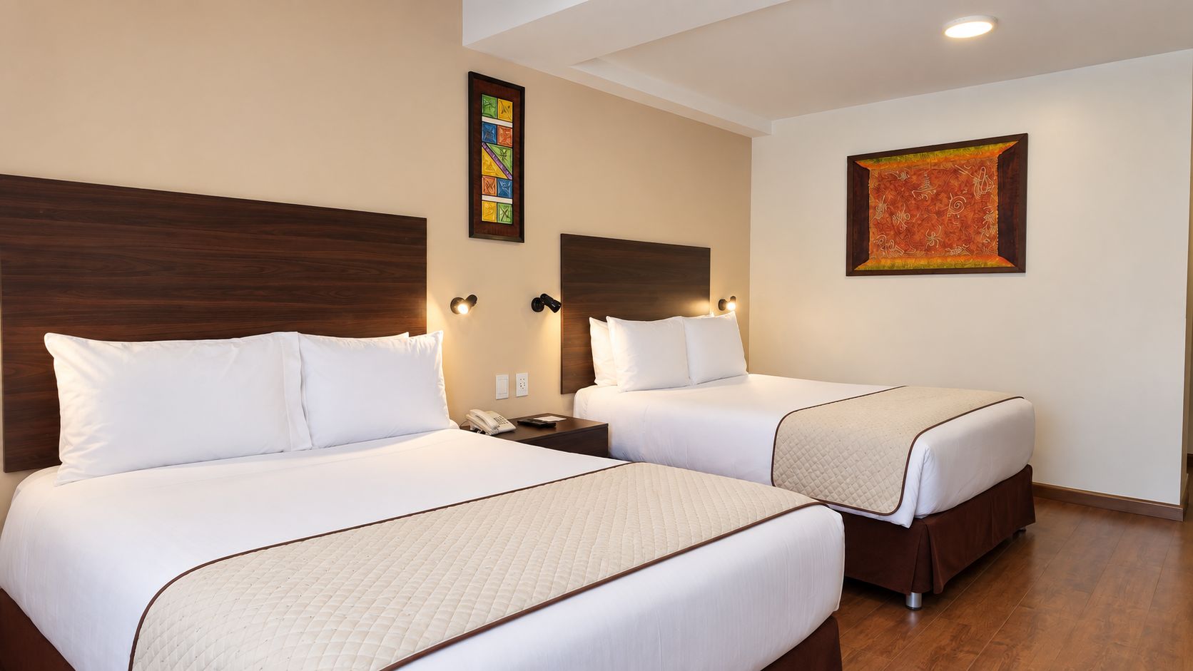 Habitación de hotel con dos camas, una mesita de noche, un teléfono y obras de arte en las paredes.