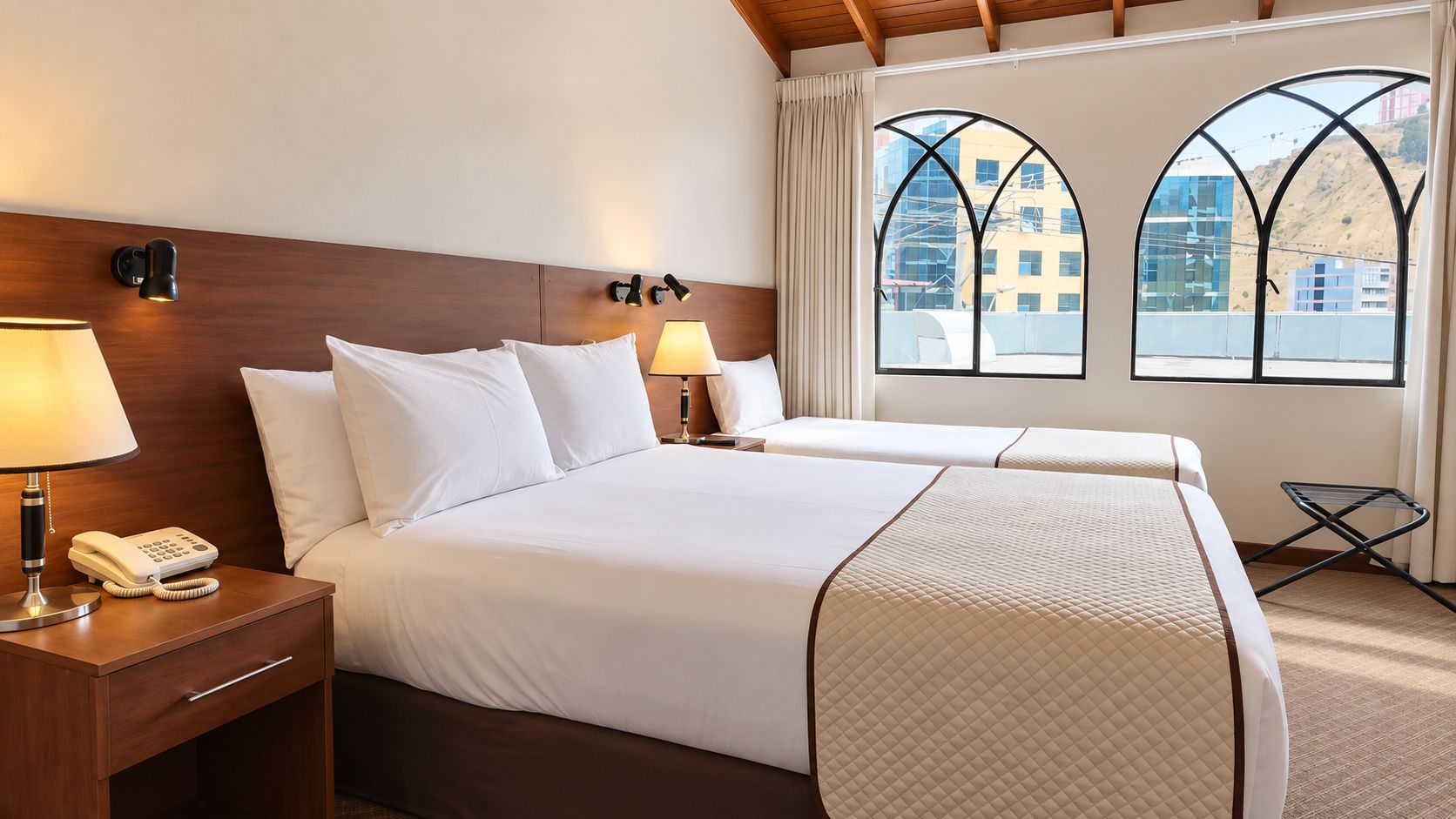 A hotel room with two beds, a nightstand with a phone, lamps, and a window with a view of buildings.