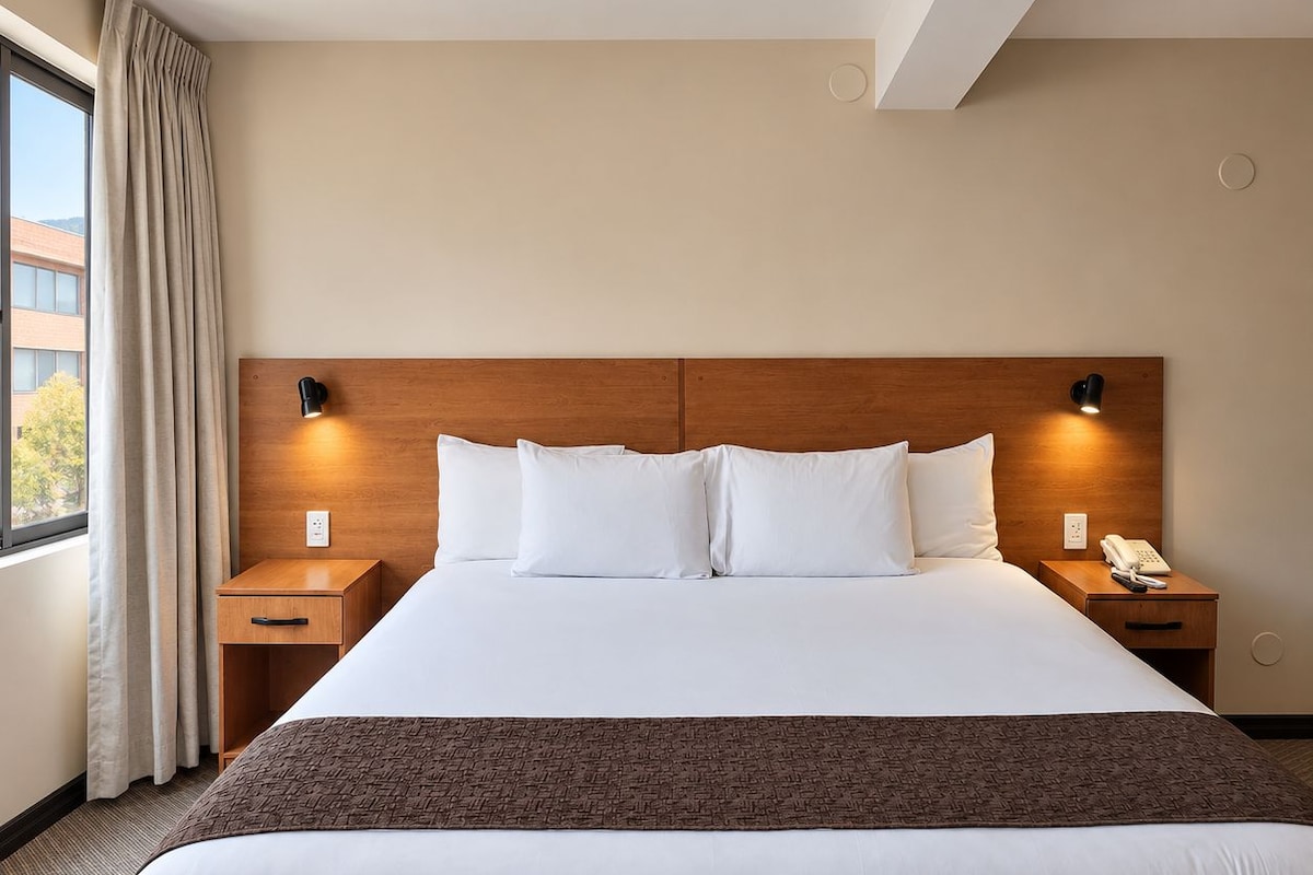 A hotel room with a large bed, two bedside tables, a telephone, and a window with curtains.