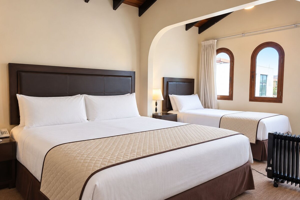 Ein Hotelzimmer mit einem großen Bett, einem kleineren Bett, einem Nachttisch mit Lampe, einem Telefon und einem Heizkörper.