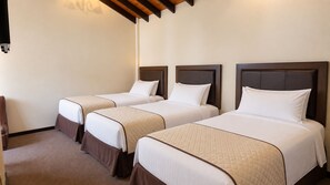 A hotel room with three single beds, each with a headboard, a bedside table, and a chair. - Hotel Calacoto (La Paz)