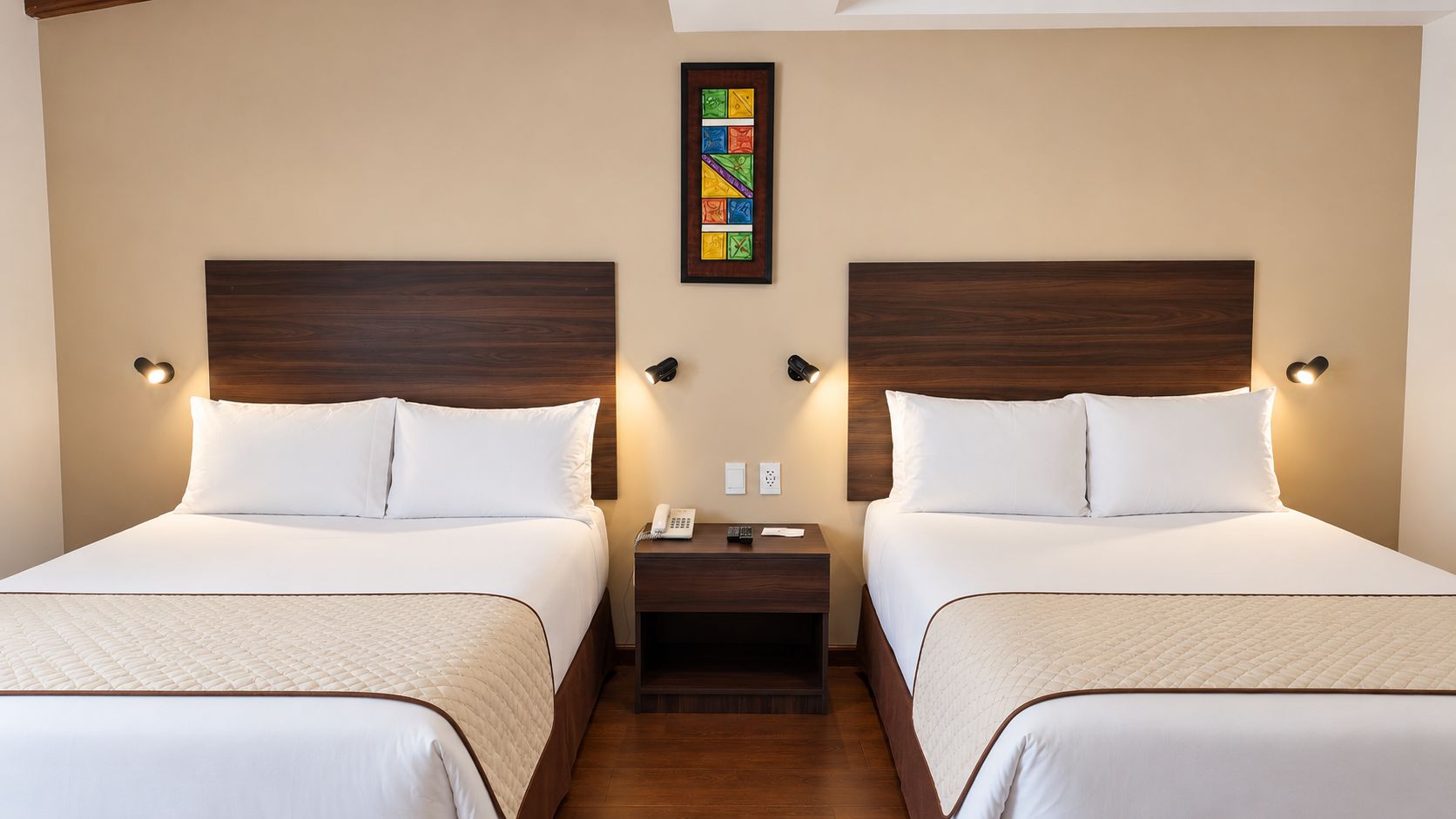 Habitación de hotel con dos camas, cada una con cabecero de madera, ropa de cama blanca y lámparas de noche.