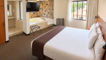 Habitación de hotel con una cama grande, baño con bañera, televisor de pantalla plana y ventana con cortinas.