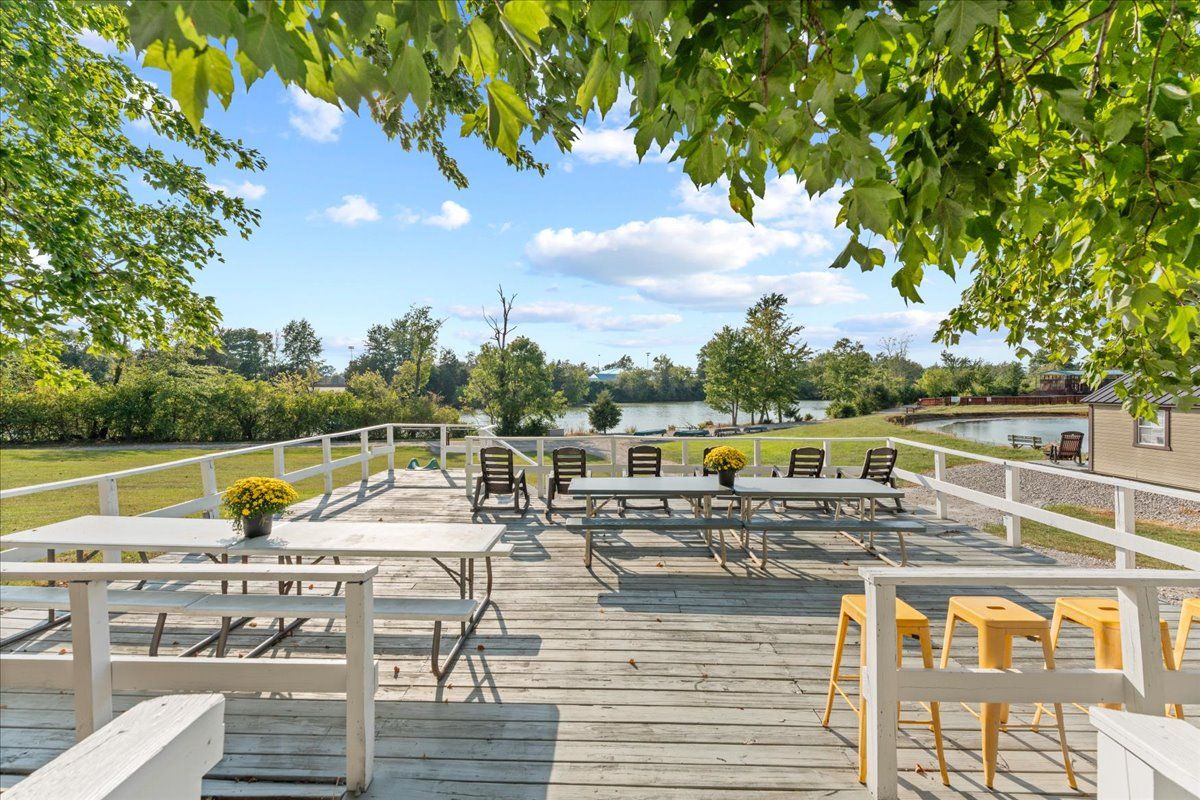 En udendørs terrasse med picnicborde og stole, med udsigt over vand og en park.