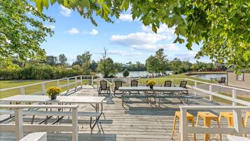 En udendørs terrasse med picnicborde og stole, med udsigt over vand og en park.