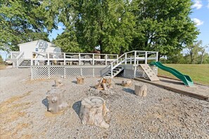 A playground with a slide, wooden stumps, and a white fence structure.