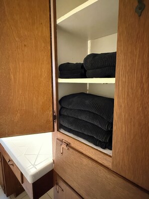 Une armoire en bois avec un matelas blanc en bas et des étagères où sont pliées des couvertures.