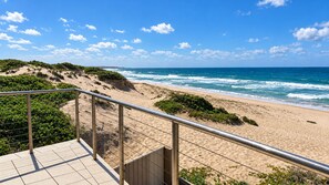 A beach with a metal railing and a tiled walkway. - The Ocean Dunes - Absolute Beachfront (The Entrance North)