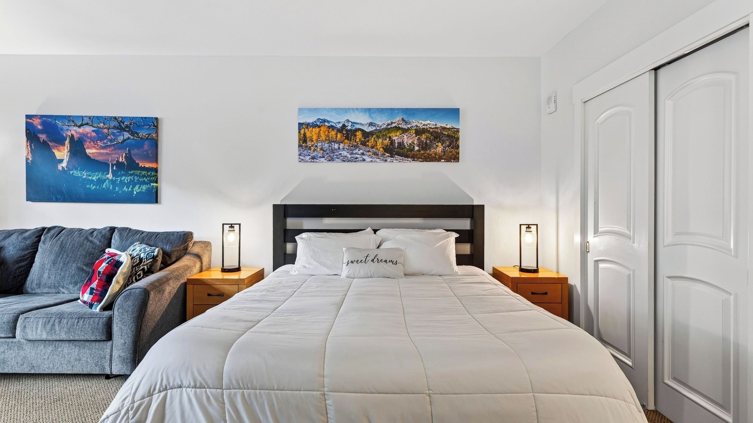 A bedroom with a bed, nightstands, a sofa, and two wall-mounted paintings.