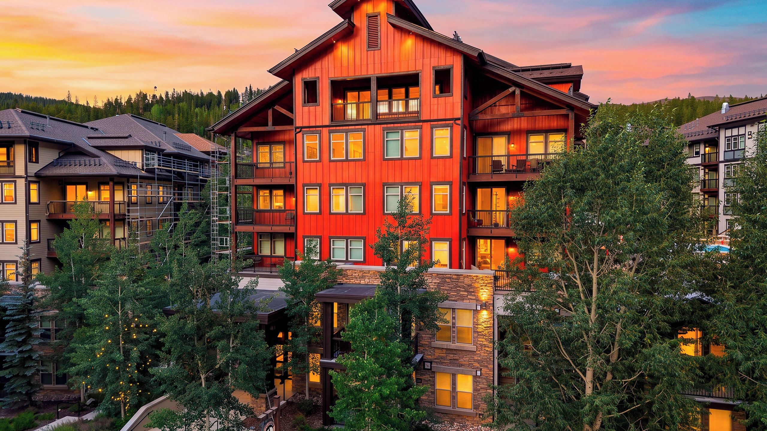 A multi-story hotel with a prominent red facade, multiple balconies, and a view of surrounding trees.
