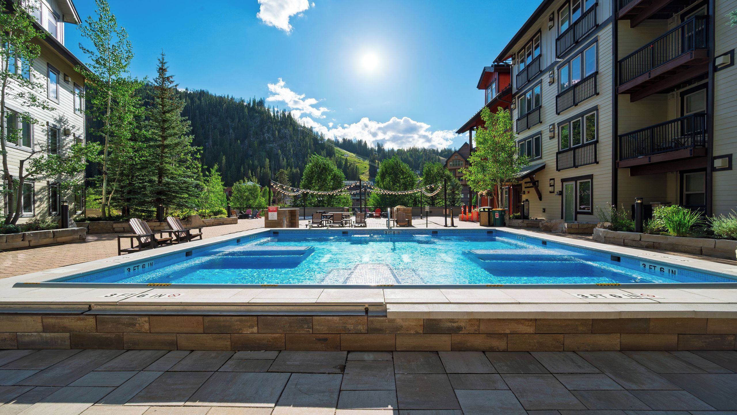 A swimming pool with a 3 ft 6 in depth, surrounded by lounge chairs and a mountainous backdrop.