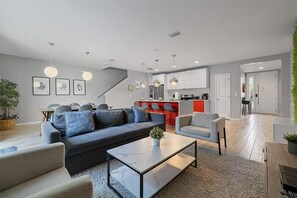 A modern living room with a sofa, armchairs, and a coffee table. There is a kitchen area with red accents and a staircase leading to another level. - Magical 4BR Home Mickey & Star Wars Rooms Pool (Kissimmee)