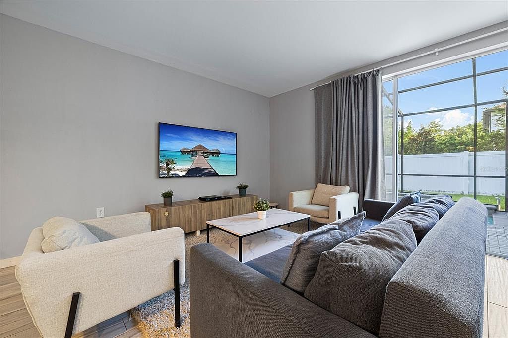 Ein modernes Wohnzimmer mit einer Couch, Sesseln, einem Couchtisch und einem Bild einer tropischen Szene.