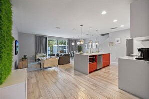 A modern kitchen with a central island, a dining area with a sofa and chairs, and a living room with a couch and a coffee table. - Magical 4BR Home Mickey & Star Wars Rooms Pool (Kissimmee)