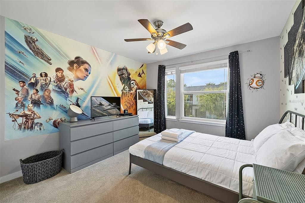 Ein Schlafzimmer mit Bett, Schreibtisch, Deckenventilator, Fenster mit Vorhängen und einer Wand mit Wandgemälde zum Thema Weltraum.