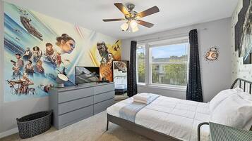 Ein Schlafzimmer mit Bett, Schreibtisch, Deckenventilator, Fenster mit Vorhängen und einer Wand mit Wandgemälde zum Thema Weltraum.