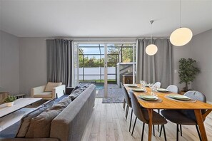 A modern dining area with a wooden table set for four, a sofa, and a view through a glass door to an outdoor space. - Magical 4BR Home Mickey & Star Wars Rooms Pool (Kissimmee)