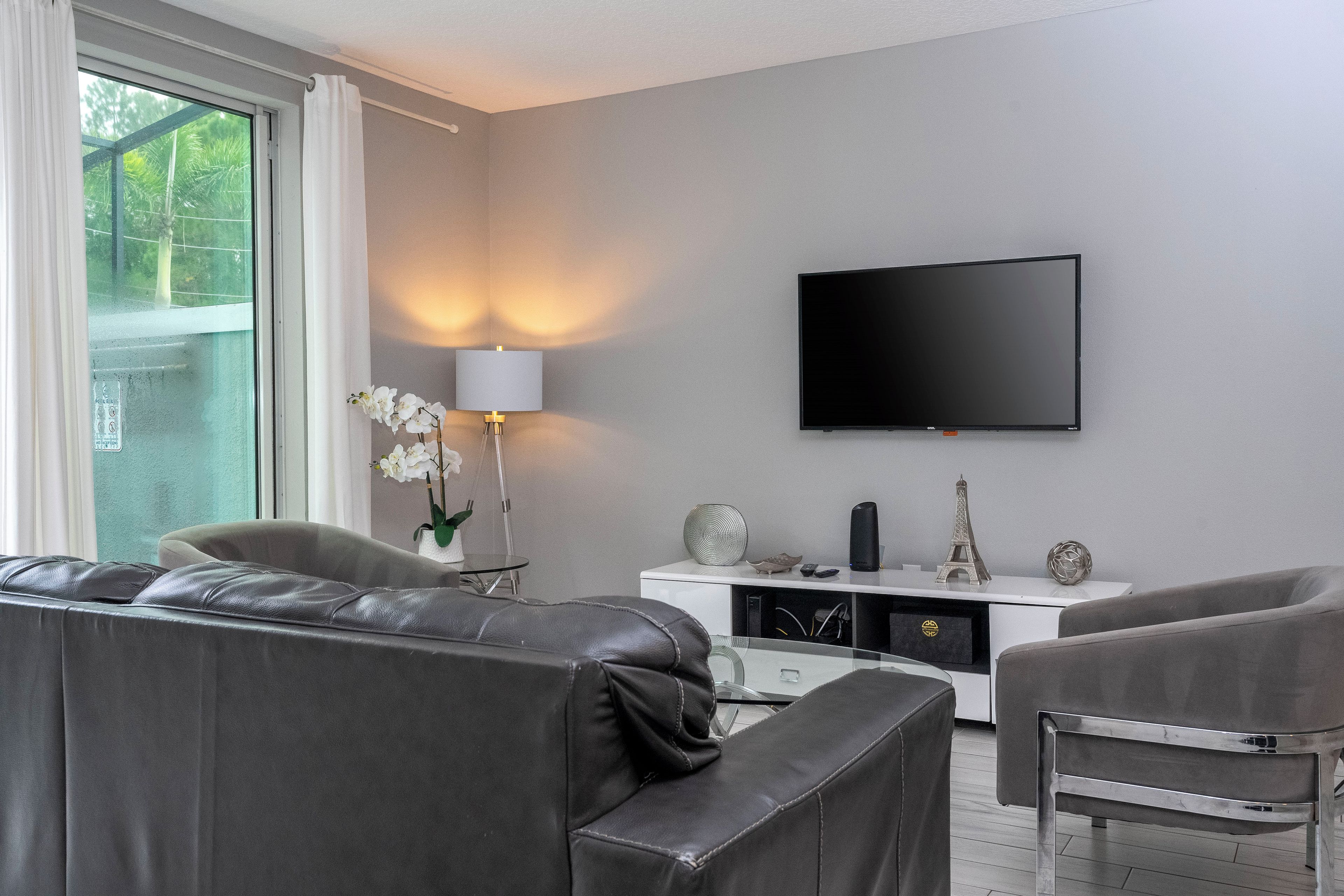 A modern living room with a grey sofa, a white entertainment unit with a flat-screen TV, and a lamp.
