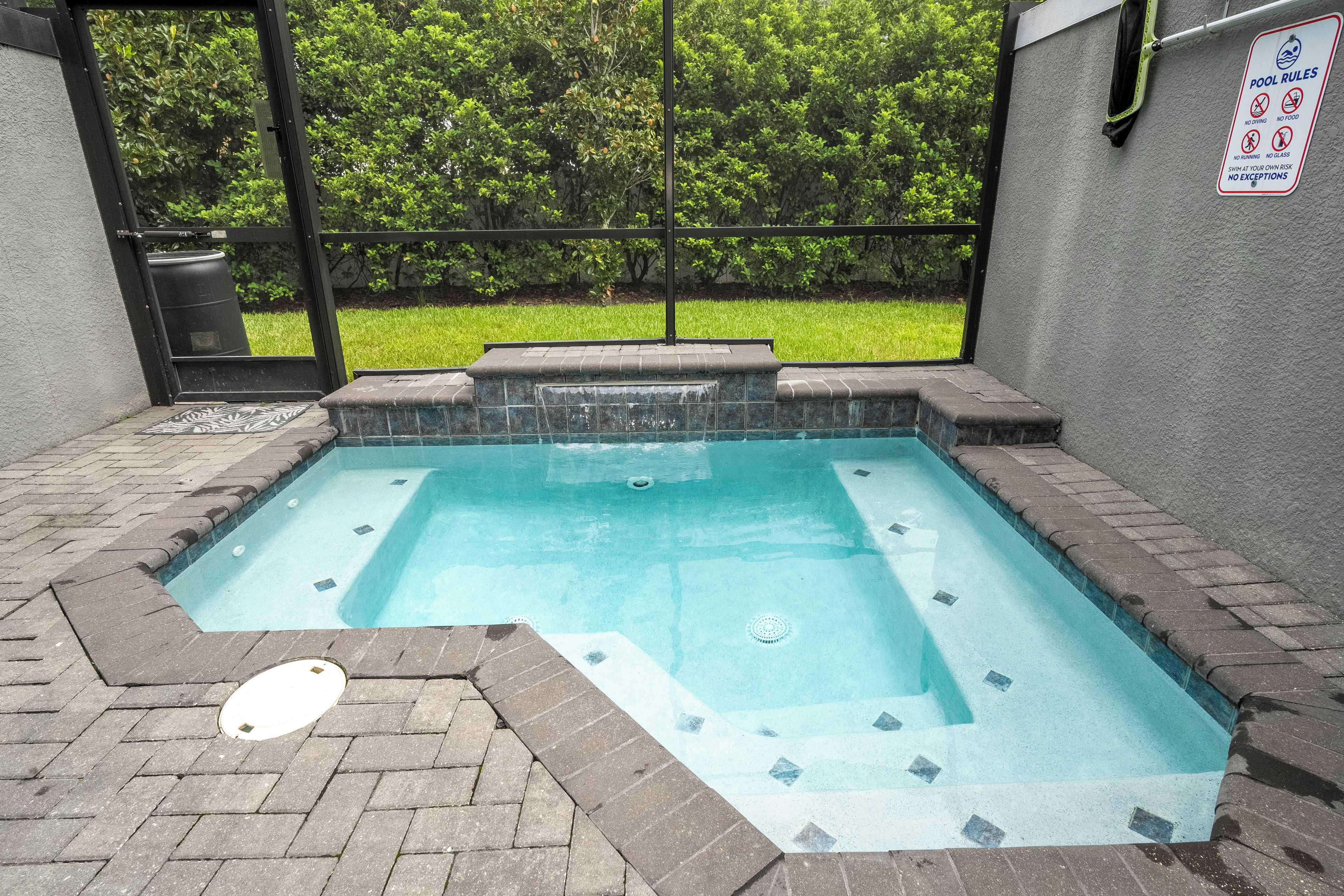Ein rechteckiger Pool im Freien mit einer gefliesten Kante, umgeben von einer Ziegelmauer und einem Metallzaun.