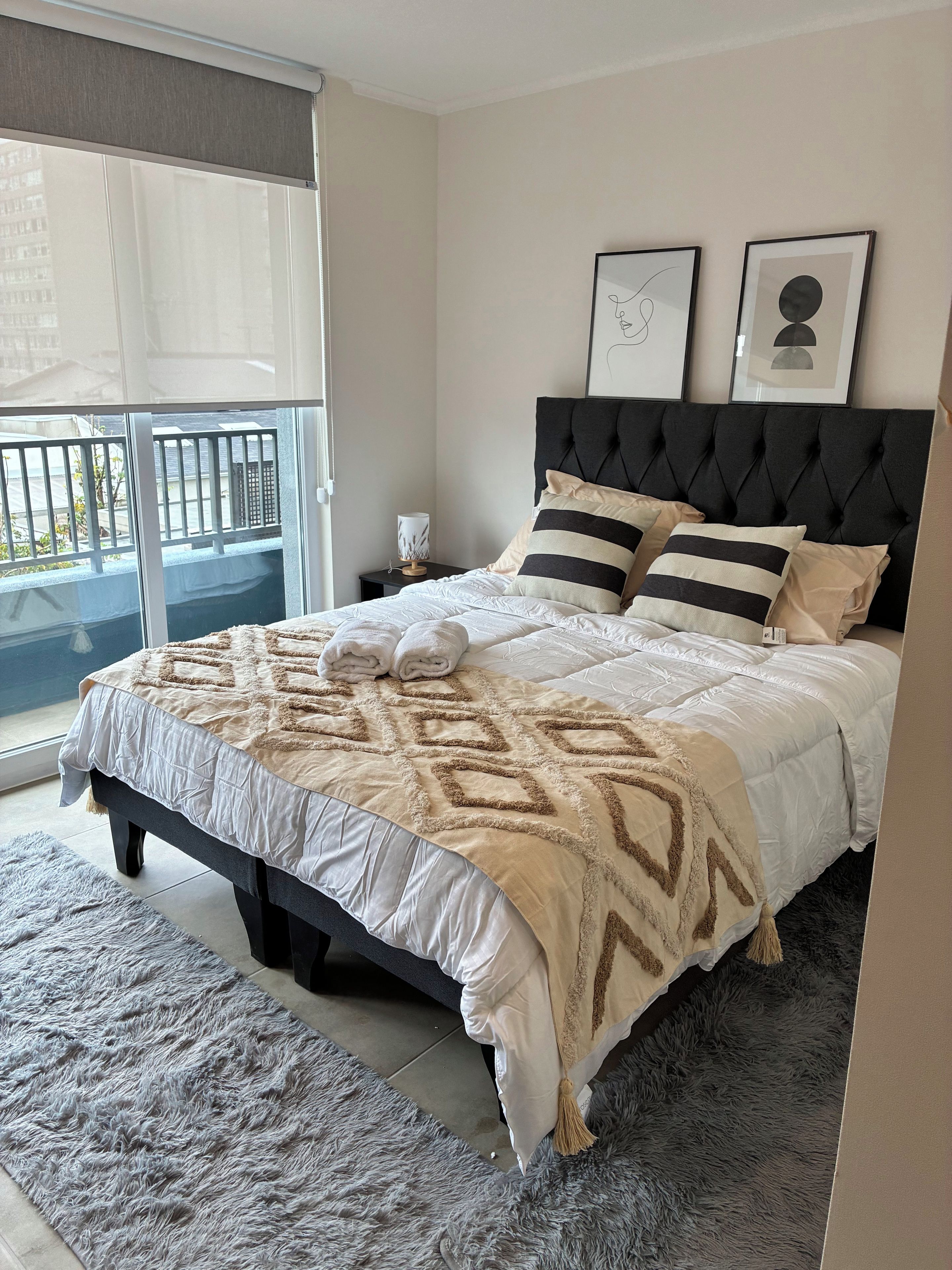 A bedroom with a bed, pillows, a nightstand, a lamp, and a view through a window.