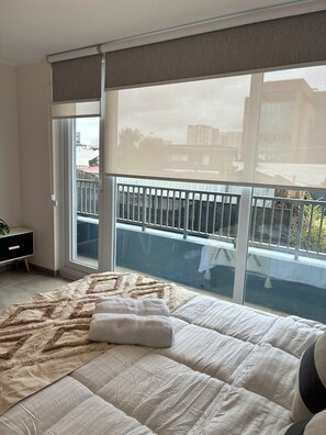 A bedroom with a large bed, a window with a view of a balcony, and a small bedside table. - Enjoy a modern and cozy studio apartment in Concepción. (Concepción)